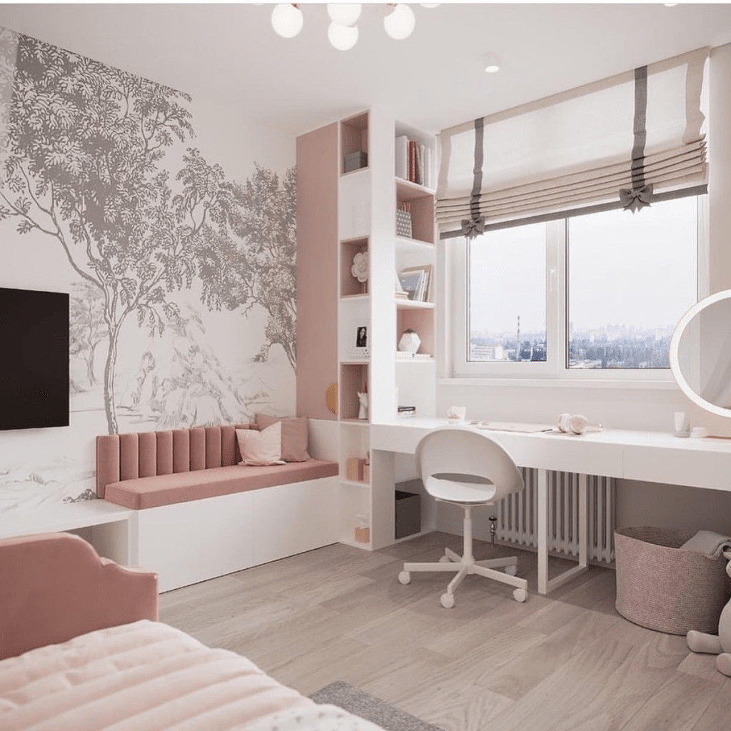 “Modern feminine bedroom with blush pink accents, wall mural with tree design, built-in desk under a large window, white shelving, and cozy seating nook with velvet bench.”