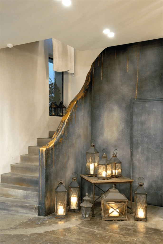 "Industrial rustic staircase with distressed wall finish, gold paint drips, and decorative lanterns with glowing candles creating a moody ambient atmosphere."