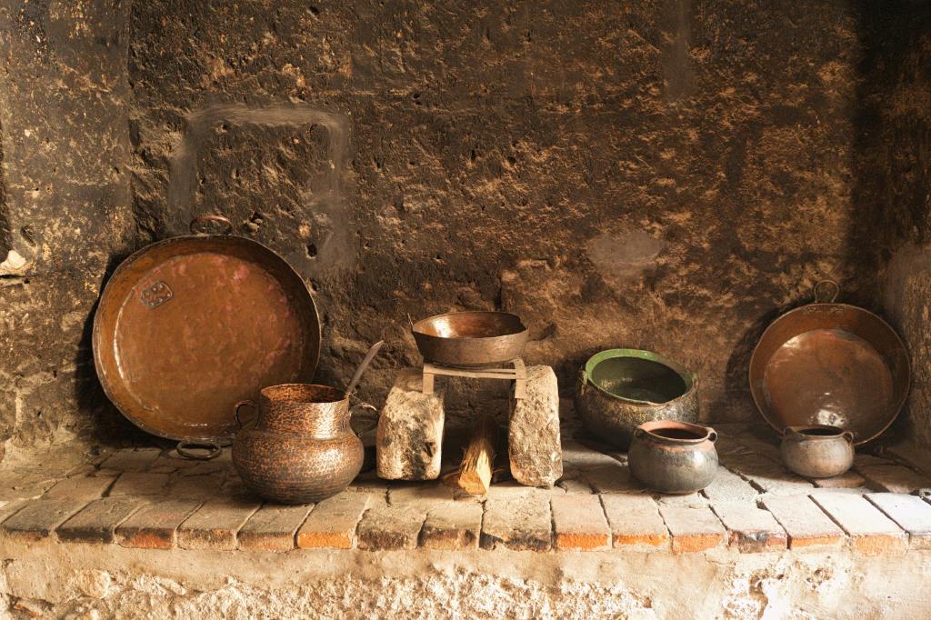 "Rustic old kitchen with traditional copper pots, clay cookware, and stone hearth, showcasing vintage cooking tools and patina finishes."