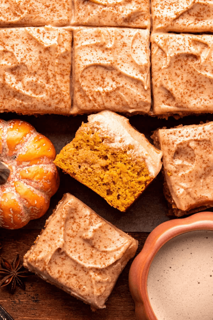 “Homemade pumpkin spice latte cake squares with cinnamon cream cheese frosting, sprinkled with nutmeg and served alongside a pumpkin and spiced latte. Moist, fluffy fall dessert perfect for Thanksgiving, Halloween, or cozy autumn baking.”