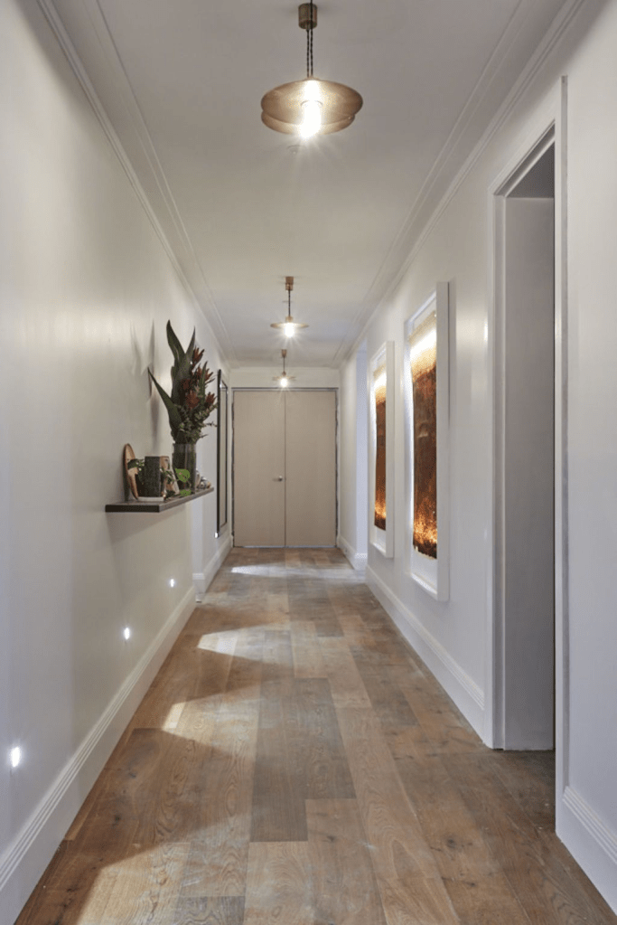 “Modern hallway with wooden flooring, recessed wall lights, and contemporary ceiling fixtures creating a warm ambient glow. Minimalist corridor design with neutral palette and subtle decorative accents for elegant interior lighting inspiration.”“Modern hallway with wooden flooring, recessed wall lights, and contemporary ceiling fixtures creating a warm ambient glow. Minimalist corridor design with neutral palette and subtle decorative accents for elegant interior lighting inspiration.”