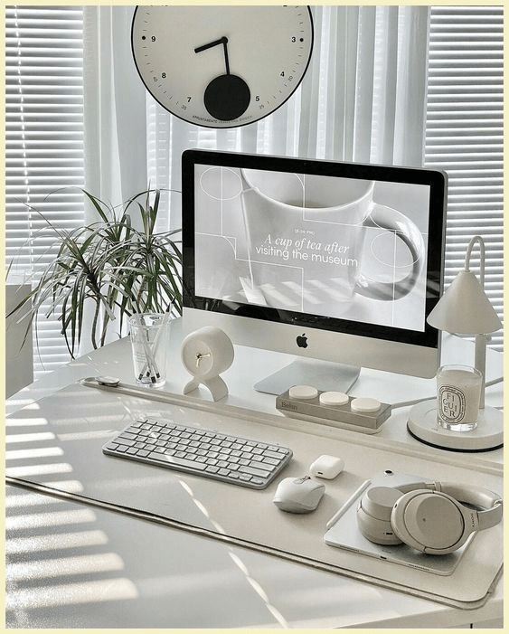 “Minimalist white home office setup with an iMac, wireless keyboard, headphones, desk accessories, and soft natural light through blinds, creating a clean and modern workspace aesthetic.”