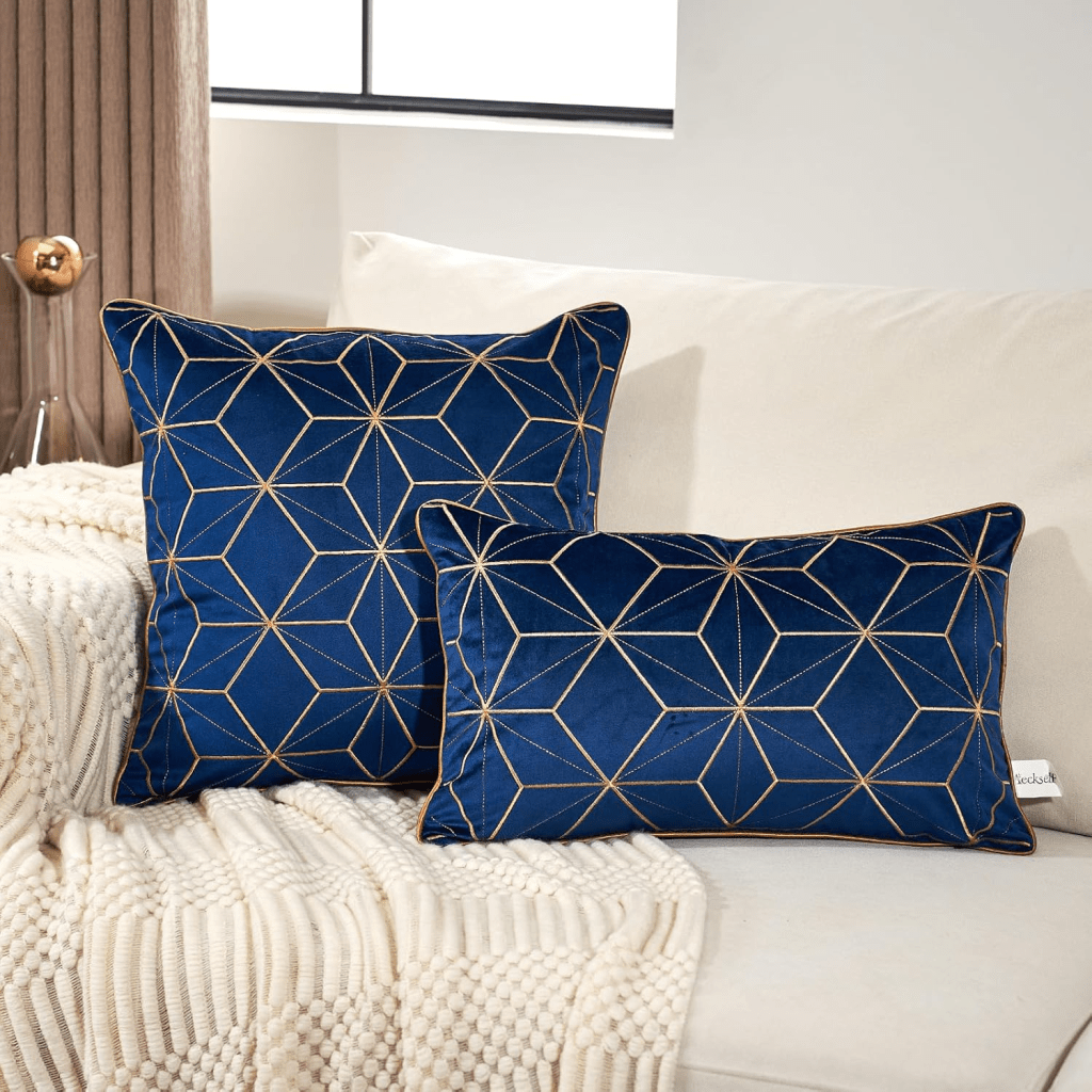 Luxury navy blue velvet throw pillows with gold geometric embroidery styled on a white sofa, modern glam living room decor with textured knit throw and elegant accent cushions.