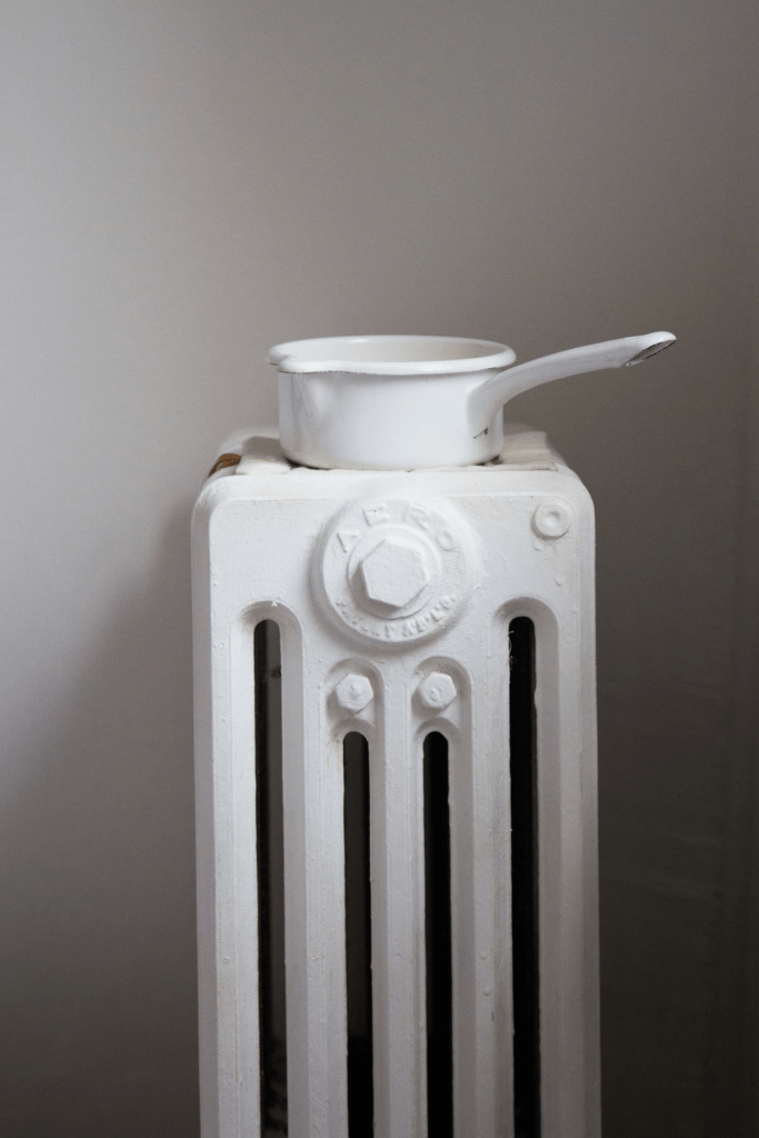 White radiator with water evaporator pan on top for natural indoor humidification, energy-efficient home heating accessory to improve air quality and prevent dry air.