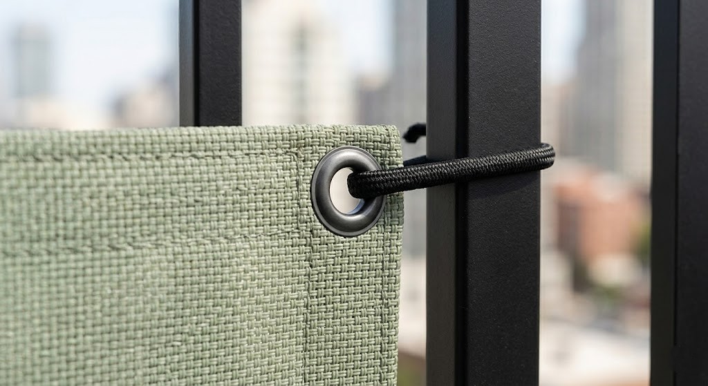 Close-up technical detail of a sage-green UV-stabilised HDPE woven balcony screen showcasing a durable marine-grade black grommet and tension cord attachment.